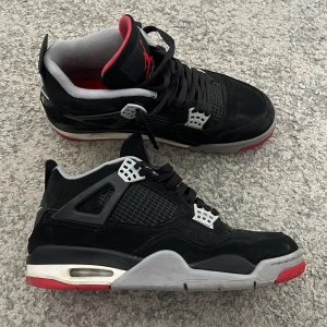 Svarta Nike Air Jordans - Säljer ett par klassiska svarta Nike Air Jordans med röda och grå detaljer. Skorna har snörning och en ikonisk design med Nike Air-logga på hälen. Perfekta för sneakerheads som vill ha en tidlös stil.