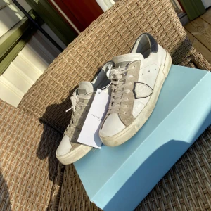 Vita sneakers från Philippe Model - STORLEK 40 MEN SITTER SOM 41.Snygga vita sneakers från Philippe Model med gråa detaljer och snörning. Skorna har en klassisk design med en bekväm sula och är perfekta för en stilren look. Levereras i originalkartong.