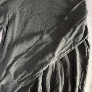 Grå långärmad tröja från Dressmann - Säljer en stilren grå långärmad tröja från Dressmann i mjuk Pima bomull. Perfekt för en avslappnad look. Tröjan har en klassisk passform och ribbade muddar vid ärmslut och nederkant.