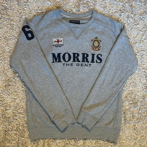 Grå sweatshirt från Morris S - Säljer en stilren grå sweatshirt från Morris med tryck på bröstet och en broderad detalj. Tröjan har långa ärmar och ribbade muddar vid ärmslut och nederkant. Tillverkad i 100% bomull. Perfekt för en avslappnad stil. Storlek S men passar säkert även M, mått skickas såklart vid osäkerhet. Postas samma dag som köp eller dagen därpå💯🙌