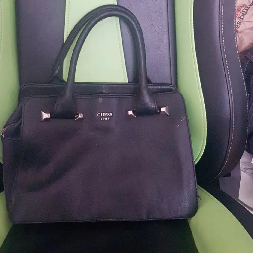 Snygg svart handväska från Guess med stilrena detaljer. Väskan har två handtag och en praktisk dragkedja upptill. Insidan är rymlig med flera fack för enkel organisering. Perfekt för att bära med sig det nödvändigaste med stil. Köpt sacond hand😁. Laukut & Käsilaukut.