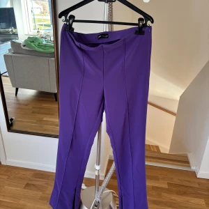 Lila byxor med dragkedja - Snygga lila byxor med dragkedja i sidan och vid benen man kan välja ha dem öppen eller stängd . Byxorna har en elegant och stilren design med en rak passform. Perfekta för att lägga till en färgklick i garderoben. 