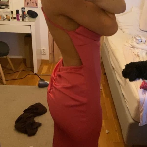 Rosa långklänning med öppen rygg - Säljer en snygg rosa långklänning med smala axelband och öppen rygg. Klänningen har en draperad framsida och korsade band i ryggen. Perfekt för en festlig kväll!