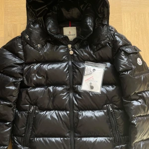 Svart äkta Moncler-dunjacka  - Äkta Moncler dunjacka i väldigt fint skick, utan defekter  Jackan har avtagbar liva, är varm, en innerficka och två framfickor med dragkedja  Storlek 3, motsvarande L Bevis finns, oöppnad NFC  Säljer för att den inte kommer till användning längre   
