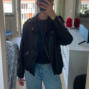 Svart skinnjacka  - Snygg svart skinnjacka med dragkedja och knappar. Stl 34 men stor i storleken. Sitter som på bilden på mig 167cm 60kg. Inte äkta skinn. 