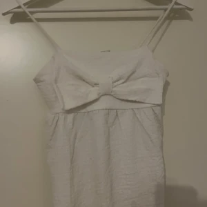 Jättefin somrig vit topp med rosett🎀✨ - Söt vit topp med smala axelband och en stor rosett framtill. Perfekt för somriga dagar. Toppen har en enkel och stilren design med en lätt textur i tyget.