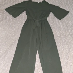 Grön jumpsuit från H&M - Snygg grön jumpsuit från H&M med vida ben och trekvartsärmar. Den har en knytning i midjan och en dragkedja bak för enkel påklädning. Perfekt för en stilren look.💞💗