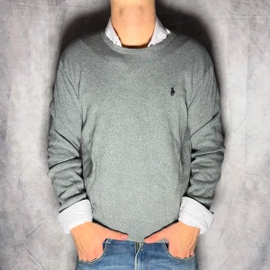 Polo Ralph Lauren tröja - Säljer en stilren grå tröja från Polo Ralph Lauren med rund hals och det klassiska logotypbroderiet på bröstet. Perfekt för en avslappnad men ändå snygg look. Passar bra till jeans eller chinos.