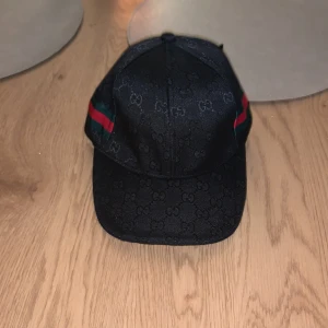Svart keps från Gucci - Säljer en svart keps från Gucci. Kepsen är diskret med  mönster och klassiska ränder i rött och grönt  för att ge din outfit en lyxig  och unik touch.Kepsen är ej använd så  fortfarande i nyskick. Går även att justera på baksidan av kepsen så passar alla passformer!  Om du är sugen på kepsen så tveka inte att höra av dig!! svarar så snabbt jag bara kan. Vid funderingar eller annat  bara att  höra av sig👊.   Självklart är priset diskuterbart!!