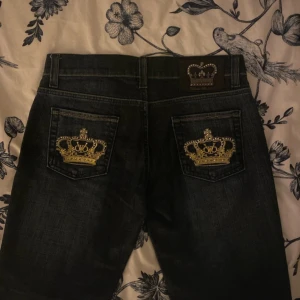 Mörkblå jeans från Victoria Beckham - Snygga mörkblå jeans från Victoria Beckham med unika guldbroderade kronor på bakfickorna. De har en klassisk femficksdesign och en knappgylf. Perfekta för en stilren look. Det står Storlek L men de är faktiskt M eftersom jag är storlek M men de är fortfarande small för mig. Jag är 166cm och har storlek M.