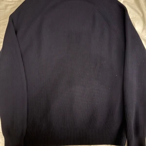 Mörkblå stickad tröja från Lacoste - Säljer en mörkblå stickad tröja från Lacoste med klassisk passform. Tröjan har långa ärmar och det ikoniska Lacoste-märket på bröstet. Priset kan diskuteras. Och nej det är inte en fläck på den. Bara skuggan