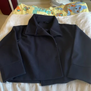 Svart kavaj från Gina Tricot - Snygg mörkblå  jacka från Gina Tricot med klassisk krage och knappar framtill. Perfekt för en stilren look. Jackan har långa ärmar och en elegant design.Endast använd ett par gånger pga felköp storlek. Nypris 600kr!!