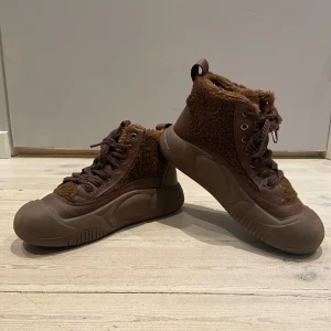 Bruna boots från Male Monkey - Snygga bruna boots från Male Monkey med snörning och en mysig pälsdetalj. Perfekta för kyligare dagar med sin robusta design och bekväma passform. De har en högre skaft och en slitstark sula.