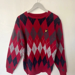 Röd rutig tröja från Lyle & Scott - Säljer en snygg röd tröja från Lyle & Scott med ett klassiskt rutmönster i svart och grått. Tröjan har långa ärmar och en liten logga på bröstet. Perfekt för en stilren look. Ny pris 1299. Prislappen hänger är fortfarande på den.