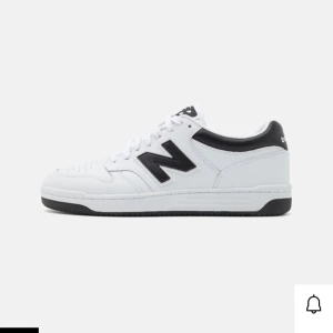 Vita sneakers från New Balance - Snygga vita sneakers från New Balance med svart logga på sidan. Skorna har en klassisk design med snörning och en bekväm sula. Perfekta för en stilren look.
