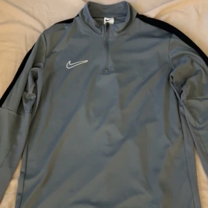 Grå långärmad tröja från Nike - Säljer en grå långärmad tröja från Nike med svart detalj på axlarna