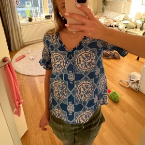 Blå mönstrad blus från Odd Molly - Säljer en super fin blå blus från Odd Molly med ett unikt mönster i vitt. Blusen har korta ärmar med volang detaljer .Perfekt till sommaren då den är lite tunnare. Säljs inte längre 