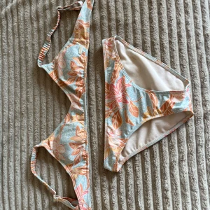 Blommig bikini i pastellfärger från Roxy - Snygg bikini med blommigt mönster i pastellfärger som blått, rosa och orange. Toppen har justerbara axelband och en enkel knäppning bak.  Storlek 12 men passar mig som har xs-s💕