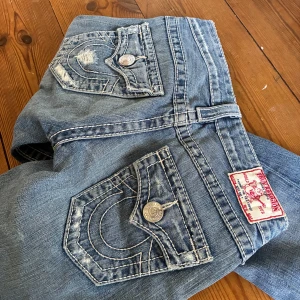 lågmidjade bootbcut jeans från True Religion 🤍 - supersnygga trueys i den gamla modellen med tjocka vita sömmar❕midja 32 cm rakt över, gren 18 o innerben 82 cm. bra skick, slitningarna tillhör design. lägg gärna prisförslag 😇