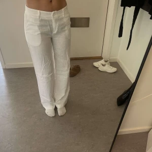 Vita linnebyxor från Design by si - Snygga vita linnebyxor från design by si med en avslappnad passform. Byxorna har en låg  midja och raka ben. Perfekta för varma dagar med sitt lätta och luftiga material. Stängs med knapp och dragkedja framtill. Passar XS-S, använda 2-3 ggr