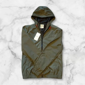 Grön jacka från Zadig & Voltaire - Snygg grön vindjacka från Zadig & Voltaire med huva och dragkedja. Jackan har elastiska muddar och en stilren design. Perfekt för den kommande våren.