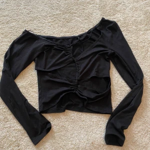 Svart långärmad topp från Only - Snygg svart långärmad topp från Only med unik design. Toppen har en v-ringad stil och dekorativa rynkdetaljer framtill som ger en cool look. Perfekt för att lyfta vilken outfit som helst.