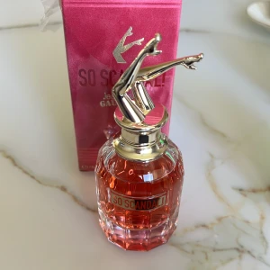 So Scandal! Parfym från Jean Paul Gaultier - Elegant parfymflaska med en unik design där locket pryds av ett par ben i luften. Flaskan är gjord av glas med en rosa ton och har en sofistikerad, feminin doft. Förpackningen är i en matchande rosa färg med märkets logotyp tydligt synlig.