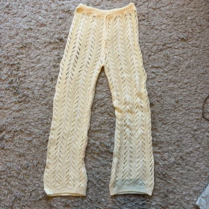 Of white stickade byxor med hålmönster - Säljer ett par of white stickade byxor med snyggt hålmönster. Byxorna har rak passform och resår i midjan för extra komfort. Perfekta för en avslappnad och trendig look eller till stranden!