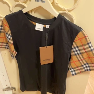 Svart t-shirt med rutiga ärmar från Burberry - Jätte snygg burberry t-shir, passar S-M. Helt ny