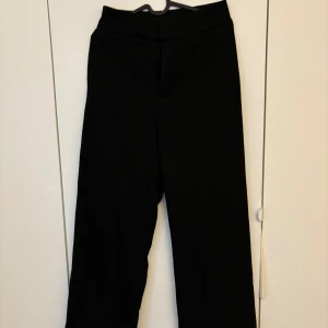 Svarta kostymbyxor från Lindex - Klassiska svarta kostymbyxor från Lindex, modell Lykke. Byxorna har hög midja och raka ben med en stilren look. Materialet känns mjukt och följsamt.