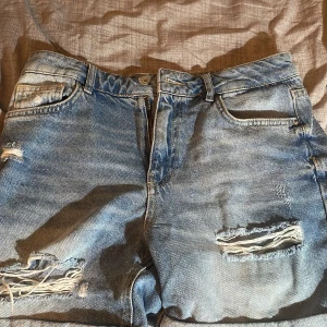 Ljusblå slitna jeansshorts från DeFacto - Säljer ett par ljusblå jeansshorts från DeFacto med slitna detaljer och råa kanter. Shortsen har klassisk femficksdesign, hög midja och uppvikta benslut. Perfekta för en avslappnad stil.