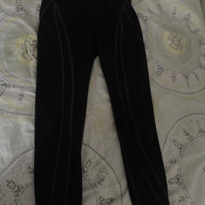 Svarta träningstights med kontrastsömmar - Svarta träningstights i storlek XS med dekorativa kontrastsömmar längs benen. Tightsen har en tight passform och är perfekta för gymmet eller löpning. Resår i midjan för extra komfort.