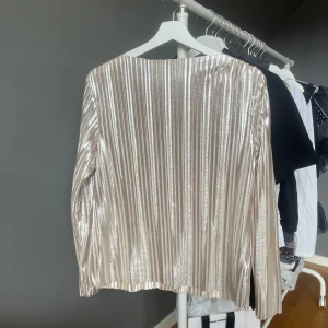 Guldig blus - Säljer en glittrig långärmad blus/topp i guld färg. Toppen har en rak passform och är perfekt för att sticka ut. Materialet är syntet och ger en snygg glansig effekt. Hör av dig vid frågor.💕