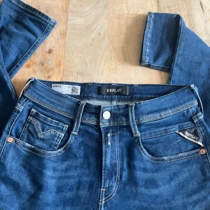 Replay jeans - Snygga blå jeans från Replay Hyperflex-serien, modell Anbass. Slim fit med klassiska fem fickor och tydliga kontrastsömmar. Märkespatch bak ochReplay-logga på fickan. Perfekta för dig som gillar stretchiga jeans med modern passform. Jeansen har ett litet märke som du ser på bild 3 men det syns knappt. Köpta på jeansbolaget för 1800 kr.