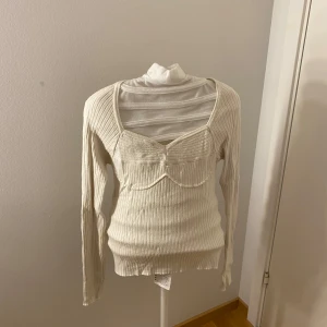 Ribbad vit långärmad topp med bystdetalj - Säljer en ribbad vit långärmad topp med markerad bystdetalj och fyrkantig ringning. Väldigt stretchigt material som sitter snyggt på kroppen, sitter fortfarande tajt. 