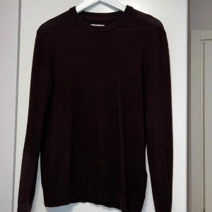 Vinröd merinoull volt tröja - En enkel och stilren vinrödstickad tröja med rund halsringning och långa ärmar. Perfekt för lager-på-lager och passar till många olika outfits. Tröjan har ribbade muddar vid ärmslut och nederkant.