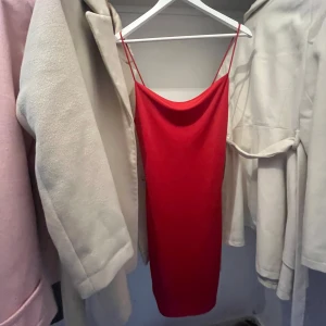 Röd klänning med smala axelband från Bik Bok - Säljer en röd klänning från Bik Bok med smala axelband och rak, tight passform. Klänningen är ärmlös och har en enkel, stilren design som passar perfekt till festliga tillfällen.