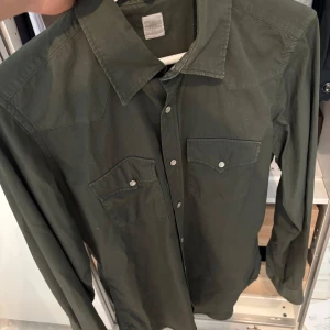 Eleventy skjorta  - Säljer en olivgrön skjorta med klassisk krage och två bröstfickor med lock och tryckknappar. Skjortan har lång ärm och är i ett mjukt bomullsmaterial. Perfekt för dig som gillar enkel och stilren look. Liknade skjortor från eleventy säljs för runt 3000-5000kr 