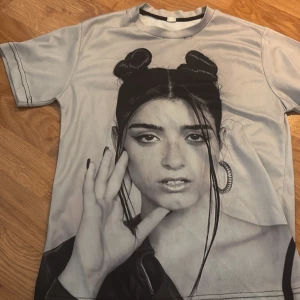 Vit t-shirt med Charlie damelio print - Cool vit t-shirt med en stor svartvit porträttbild tryckt både fram och bak. T-shirten har korta ärmar och en klassisk rund halsringning. Perfekt för dig som vill sticka ut med Charlie damelio tryck