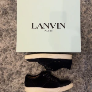Svarta sneakers från Lanvin *Kvitto - Säljer ett par svarta sneakers från Lanvin med vit sula och svarta skosnören. Skorna har en stilren design med ovandel i mocka och tåparti i skinn. Perfekta för dig som gillar lyxiga och klassiska sneakers.