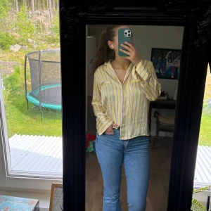 Gul och vit randig skjorta - Säljer en luftig skjorta med gula och vita ränder. Skjortan har lång ärm, klassisk krage och bröstficka. Perfekt för dig som gillar en avslappnad men ändå stilren look. Passar bra till jeans eller kjol.