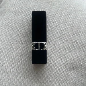 Dior Rouge läppstift 720 Icône - Säljer ett Dior Rouge läppstift i nyansen 720 Icône. Hylsan är svart med silverdetaljer och har den klassiska CD-loggan. Färgen är en elegant, dämpad rosaton med matt finish. Perfekt för dig som vill ha en lyxig känsla i sminkväskan . Kommer utan förpackning, oanvänd och otestad, om du köper fler av dessa läppstift kan jag tänka mig bättre pris. Rensning inför flytt. Vissa märken på själva skalet på läppstiftet kan förekomma då jag förvarat alla i samma låda 