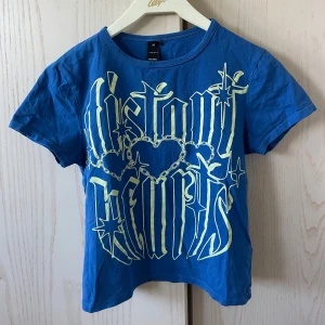 Blå t-shirt med tryck från Factorie -  blå t-shirt från Factorie med stort grafiskt tryck i vitt och gult framtill. T-shirten har rund hals och korta ärmar. Ganska croppad, sitter som en storlek S