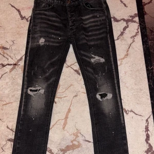 jeans från Kings Will Dream - Säljer ett par svarta jeans från Kings Will Dream med slitningar och hål på benen. Jeansen har en smal passform och klassisk femficksdesign. Snygga detaljer med slitna partier och diskreta färgstänk för en trendig look. Köpte för originalt 3000kr men säljer för mindre