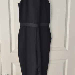 Svart ärmlös onepiece - Säljer en svart onepiece med breda axelband och markerad midja. Byxorna har en stilren design och är ärmlös, vilket ger en elegant siluett. Perfekt för dig som gillar minimalistisk stil. Storlek är mer 36 än 38