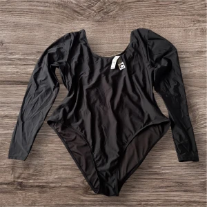 Svart långärmad baddräkt från Cubus X Philippa Parnevik  - Säljer en svart stilren långärmad baddräkt. Petfekt för både simning och strandmode. Öppen ryggdesign med knytning vilket ger baddräkten feminin och justerbar passform.