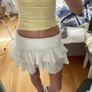 Vit volangkjol med resårmidja - Supersöt vit kjol med bred smockresår i midjan och dubbla volanglager. Kjolen är kort och har en luftig känsla, perfekt för varma dagar. Materialet är lätt och krinklat vilket ger en avslappnad vibe. Går att vika upp om man vill få den kortare. Står inte märke eller storlek men skulle gissa att de är storlek S. Hör av dig om du har några frågor eller funderingar 💕