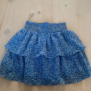 Blå blommig volangkjol från Pigalle / only  - Supersöt blå kjol från Only med vitt blommönster och volangdetaljer. Kommer inte till användning 