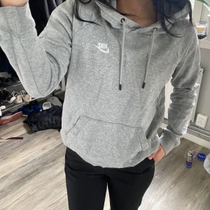 Grå hoodie från Nike - Säljer en klassisk grå hoodie från Nike med vit logga på bröstet. Tröjan har huva och en stor magficka. Perfekt för en avslappnad stil och enkel att matcha med det mesta.