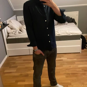 Mörkblå skjorta från East West - Snygg mörkblå skjorta från East West med klassisk krage och vita knappar. Skjortan har lång ärm och en stilren, enkel design som passar perfekt till jeans eller chinos. Fast pris.